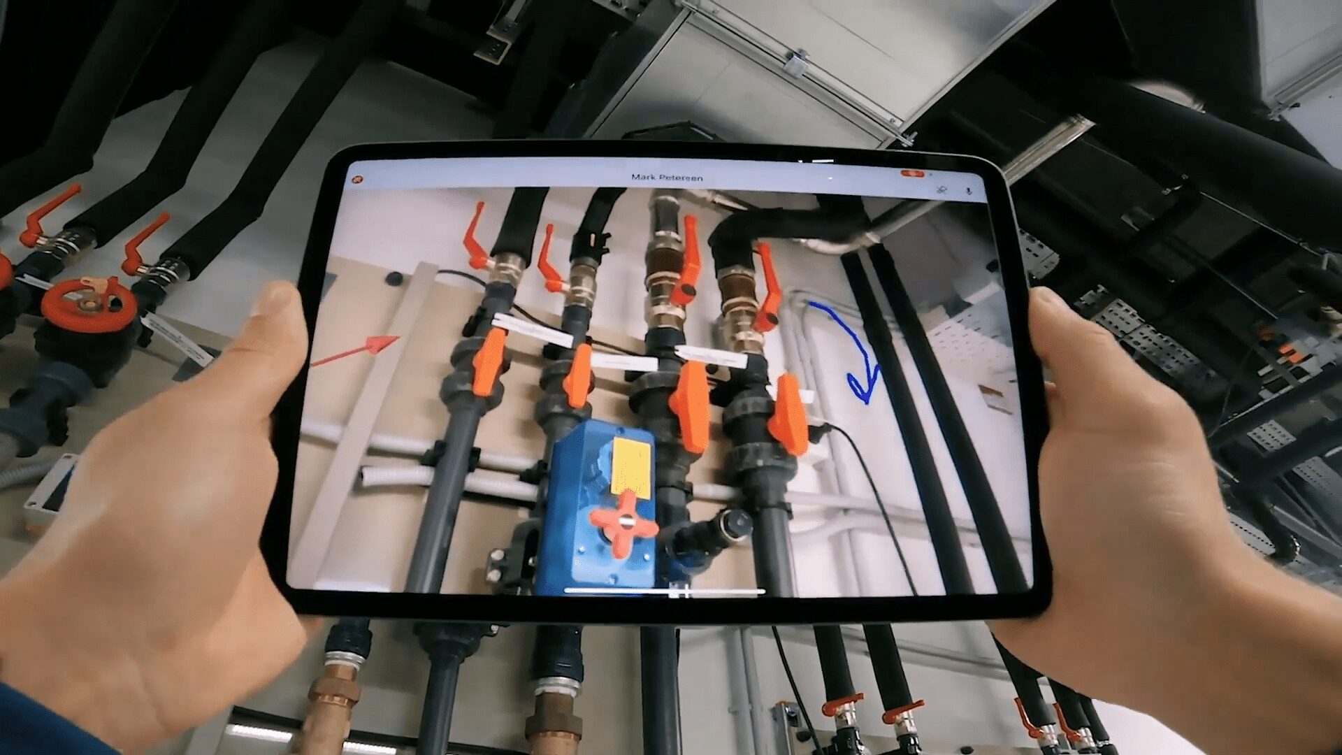 A technician using tablet running camera and pointing to pipes